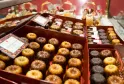Assortiment de cannelés bordelais et autres pâtisseries fines présentés dans des boîtes rouges avec étiquettes, exposés en vitrine de pâtisserie.