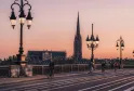 Vue au coucher de soleil du pont de pierre avec la flèche Saint-Michel en arrière-plan à Bordeaux, avec des cyclistes et des lampadaires ornementaux