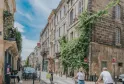 Rue Ramonet à Bordeaux Chartrons, rue pavée avec immeubles en pierre de taille, façades recouvertes de lierre, piétons et cyclistes, ciel bleu.