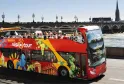 Bus touristique rouge à impériale Visi'Tour circulant à Bordeaux devant le pont de Pierre et la cathédrale Saint-Michel