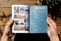 Guide touristique ouvert montrant une page avec une carte de la Gironde et des photographies de destinations, tenu à la main sur une table en bois avec des plantes vertes
