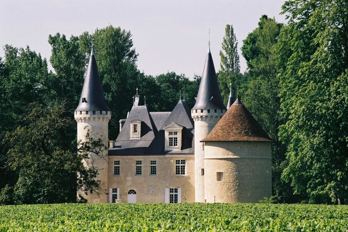 Château de style Renaissance avec tours pointues et toits coniques, entouré de verdure et de vignobles en Bordelais