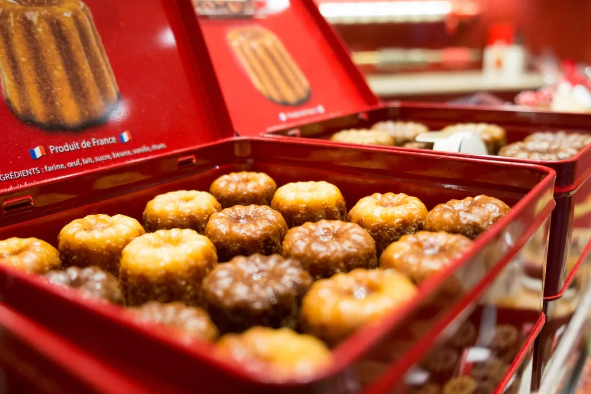Boîte rouge ouverte contenant des canelés bordelais dorés saupoudrés de sucre, produit français traditionnel de Bordeaux