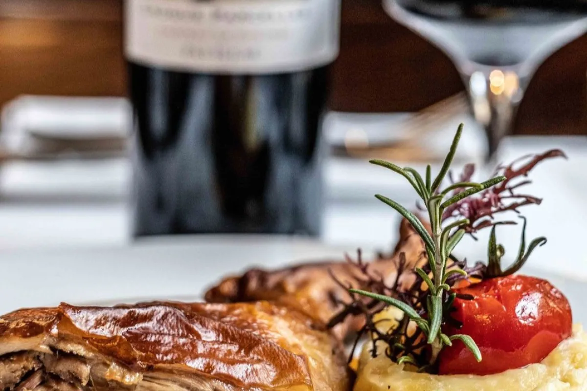 Assiette de viande rôtie avec purée de pommes de terre, tomate rôtie et romarin, accompagnée d'une bouteille de vin rouge de Bordeaux et d'un verre de vin dans un restaurant traditionnel bordelais.