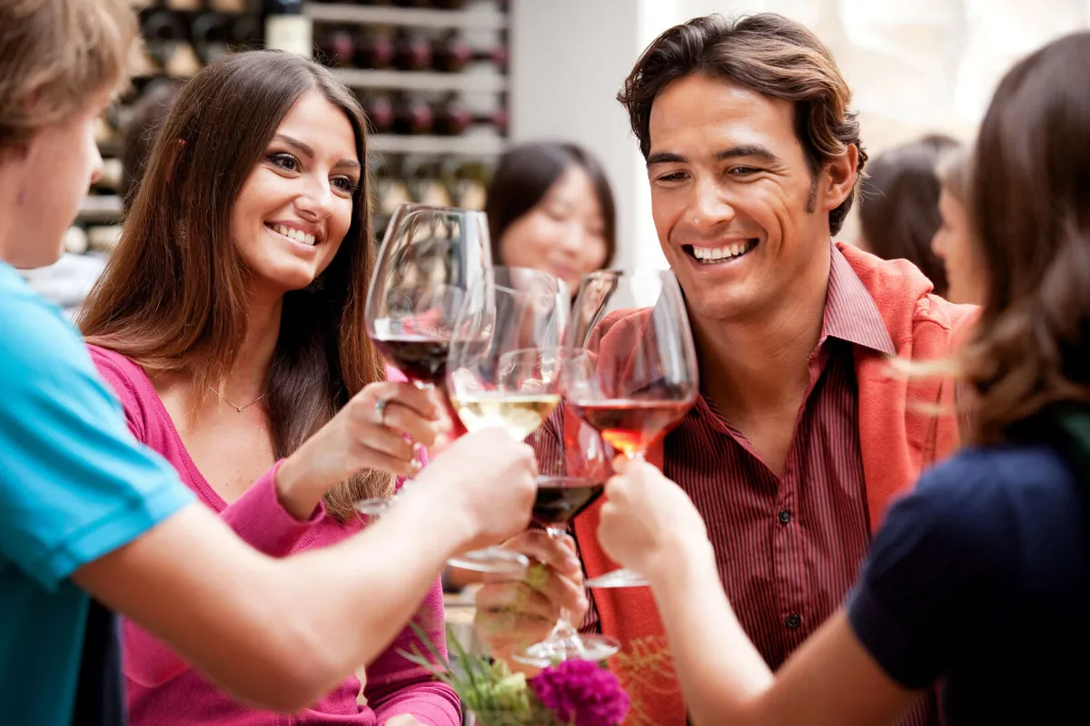 Un groupe de personnes souriantes dégustant du vin rouge et blanc lors d'une réunion conviviale dans un bar à vin de Bordeaux.