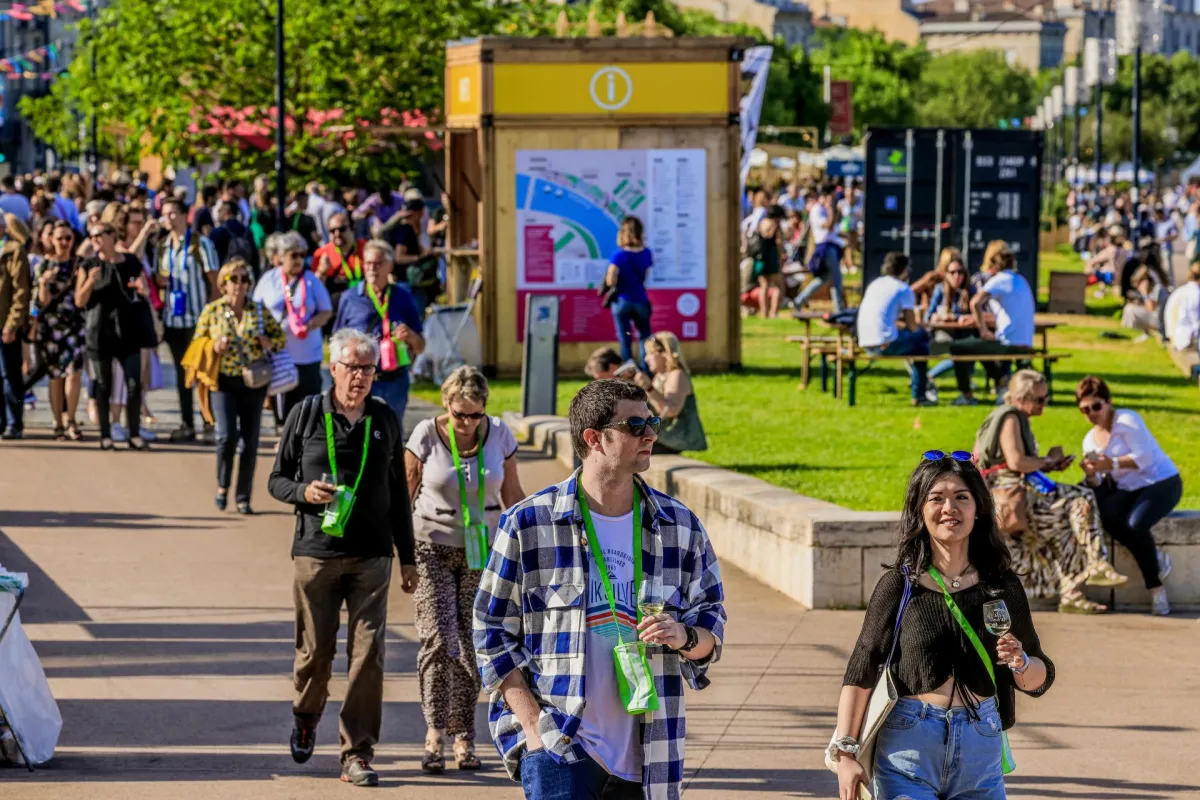 Foule de visiteurs portant des badges verts lors d'un événement à Bordeaux, avec un plan d'information jaune visible et des espaces verts en arrière-plan.