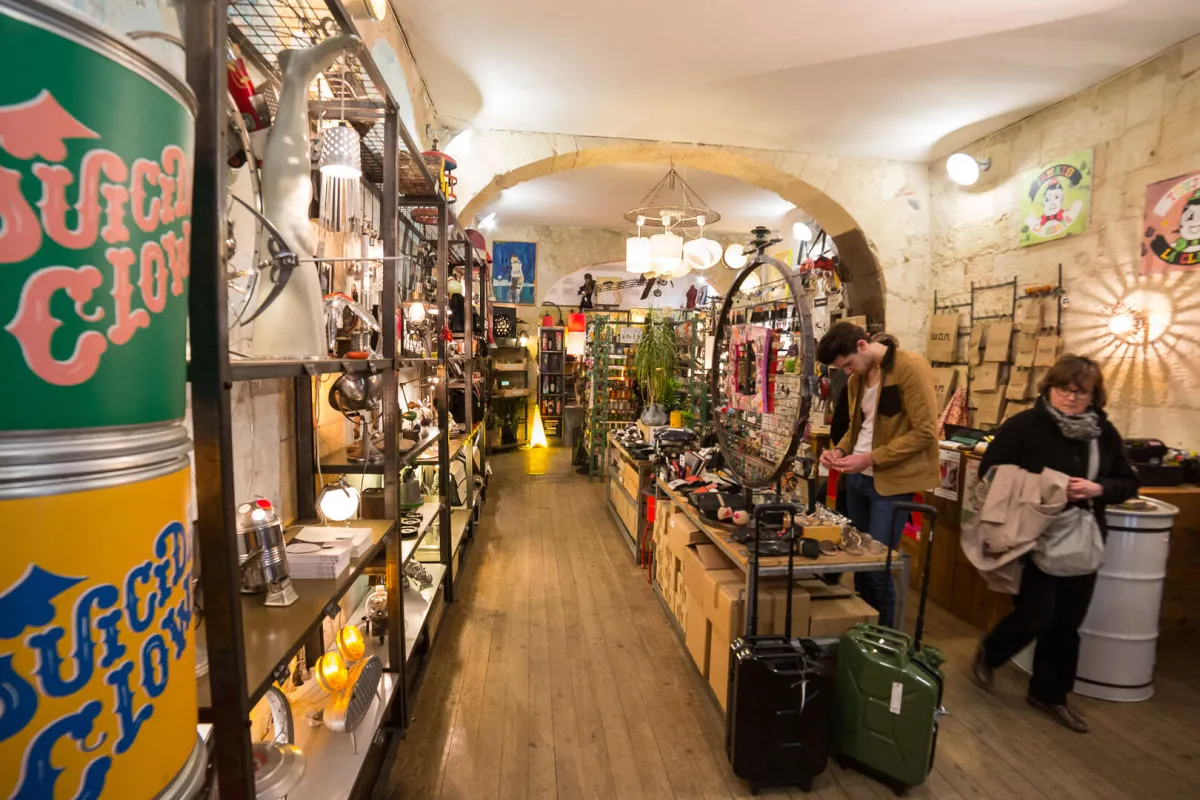Intérieur d'une boutique de souvenirs bordelaise présentant des objets artisanaux et locaux sur des étagères, avec des visiteurs parcourant les produits typiques de Bordeaux.