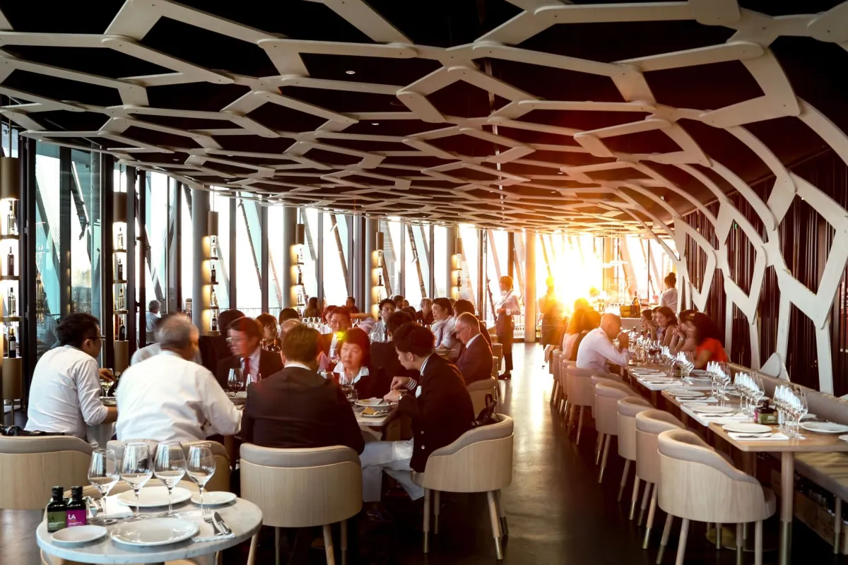 Cette photo présente la salle du restaurant Le 7 à la Cité du Vin. De nombreuses personnes sont en train de manger. 
