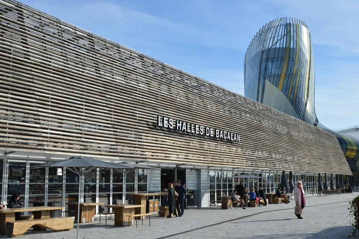 Façade moderne des Halles de Bacaean à Bordeaux avec architecture contemporaine aux lignes ondulées, terrasse extérieure et accès aux boutiques de shopping gourmand